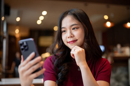 Close up pretty asian woman holding looking at smartphone resting head on hand while sitting in...