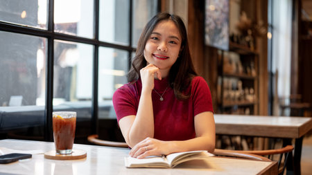 Asian woman resting head on hand and holding notebook aside coffee sitting at marble table in a...