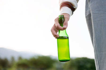 Close up of a hand holding green bottle while standing in outdoor field under bright clear sky....