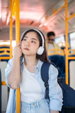 Bored asian woman tourist wear headphone while standing and holding hugging handrail in shuttle bus....