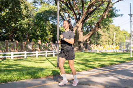 Pretty asian woman in sportswear exercising by running or jogging on the road in park under...