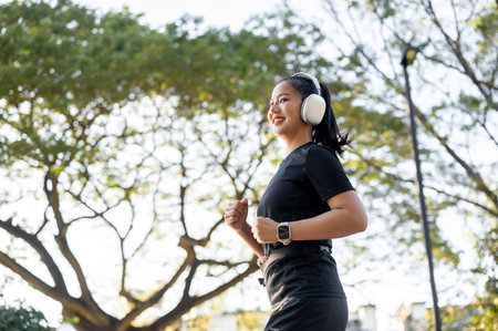 Asian woman in sportswear wearing headphone listening to music as running jogging exercising in park. Healthy Living, Working out, Urban Modern Lifeの写真素材