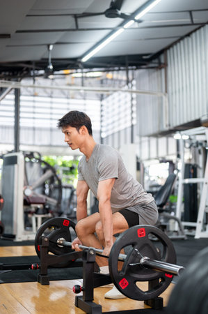 Asian man client in sportswear crouching down holding barbell exercising doing weight lifting in...