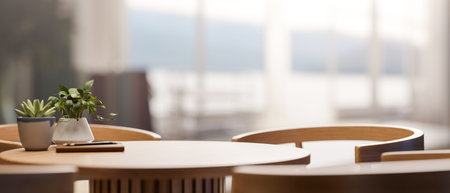 Pencil on book and potted plant vase on round wooden table and armchair in a cafe with bright...