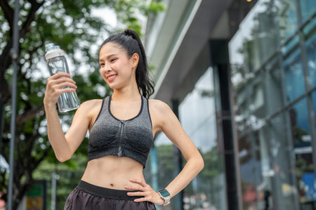 Asian woman in sportswear holding looking at water bottle with hand on waist resting after exercise....