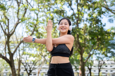Asian woman in sportswear listening to music in headphones stretching muscle before exercise in...