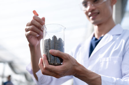 Glasses asian agricultural scientist man holding beaker testing planting soils in a greenhouse farm....