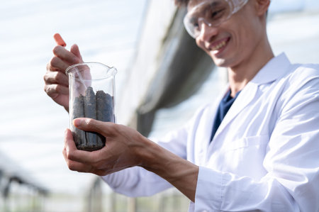 Glasses asian agricultural scientist man holding beaker testing on planting soils in greenhouse...