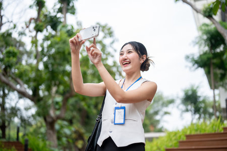 Happy asian woman office worker holding smartphone taking photos while standing on stairs in park....