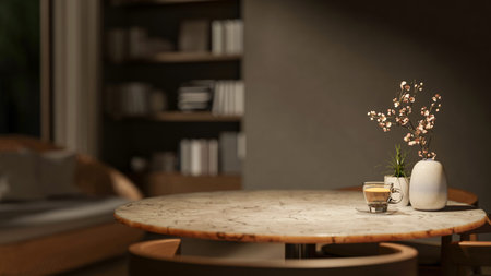 Coffee cup with potted plant and flower vase on round marble table with sofa and bookshelf in dim...