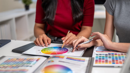 Close up of a woman and coworker holding pencil pointing on color chart sitting at table in office....