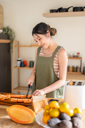 Asian woman wearings apron using knife cutting papayas on chopping board at kitchen cooking counter. Healthy Foods, Homemade meals, Balanced Living.の写真素材