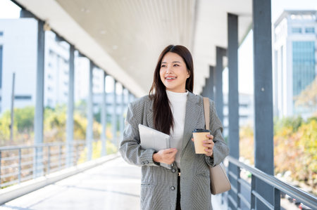 Pretty asian woman student office worker holding coffee with tablet while walking on the footbridge....