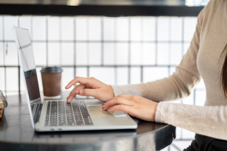 Close up of a woman's hands typing on laptop aside coffee cup while sitting at round table in cafe....