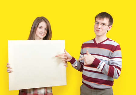 Young smiling boy and girl with poster over yellowの写真素材