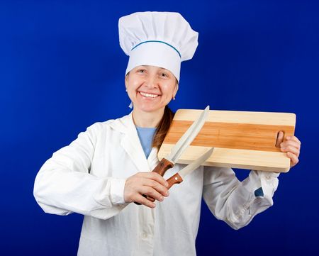 Woman in chef uniform holding cutting board and knives over blue background.の写真素材