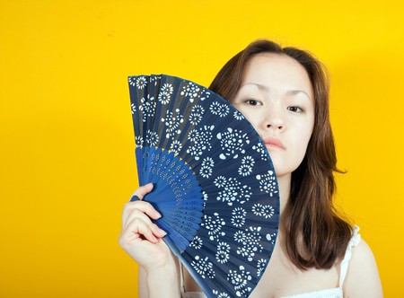 Photo of an attractive asian girl with fan  over  yellowの写真素材