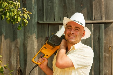 Adult  farmer standing in farm field with  chainsawの写真素材