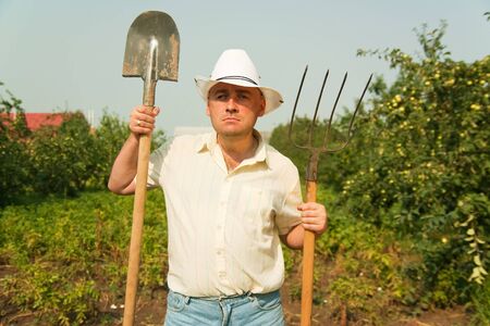 farmer holding pitchfork and spade standing in a field の写真素材