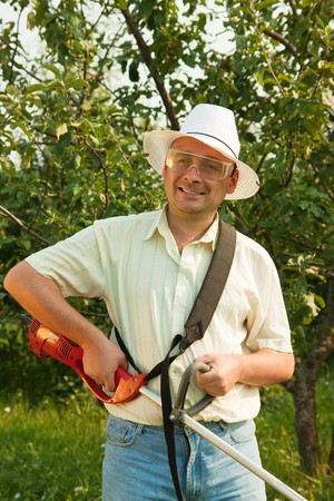 A man works with cordless grass trimmer in garden