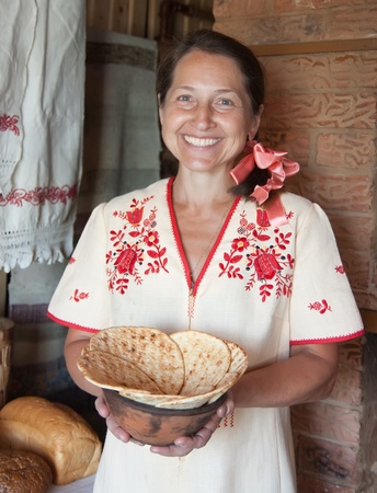 Happy mature woman with bread near traditional russian stoveの写真素材