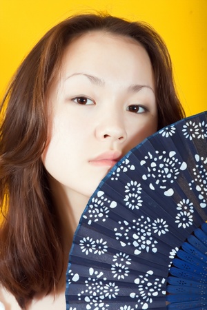 Photo of asian young woman  whith blue fan  against a yellow backdropの写真素材