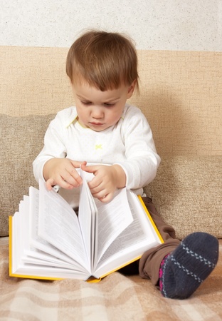 little toddler with a book sitting on sofaの写真素材