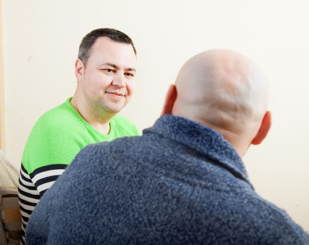 man sitting on sofa at home and talking with another manの写真素材