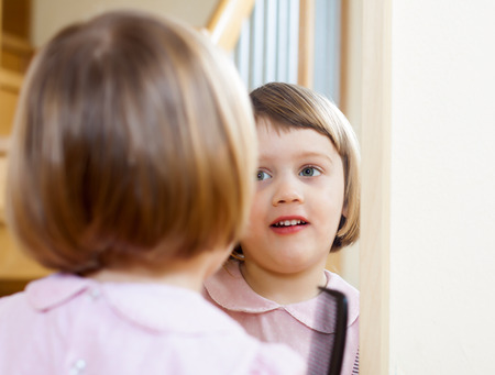 three year old child brushing her hair front of  mirrorの写真素材