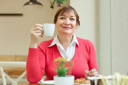 Elderly woman sitting in   cafe with   cup of coffee and   bun.の写真素材