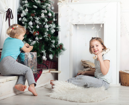 Little sisters sitting on   floor near   Christmas tree.の写真素材