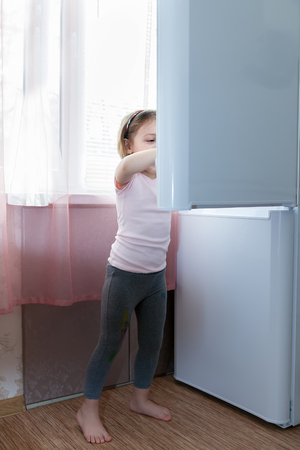Little girl standing near   refrigerator.の写真素材