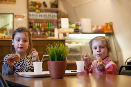 Two girls 7 and 4 years old eating donuts in   cafe.の写真素材