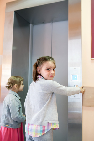 two girls near   elevator clicking on  call buttonの写真素材