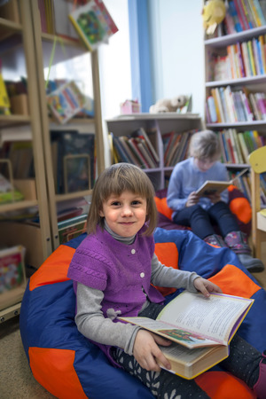  Little girl with book between shelves in library.の写真素材