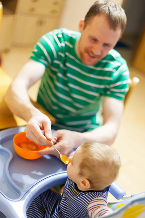 Dad giving fruit lure for baby   in   highchair.の写真素材
