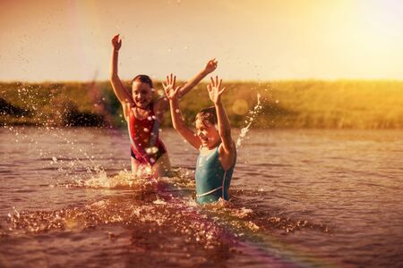 little girls in colored swimsuits splashing in   river  in   villageの写真素材