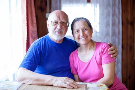 Elderly husband and wife sitting at   table at home.
