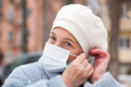 Elderly woman in winter clothes and medical mask on street. The theme of protection during an...