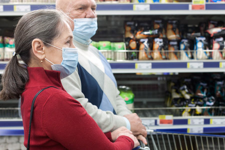 Elderly couple wearing protective masks choosing products in supermarketの写真素材