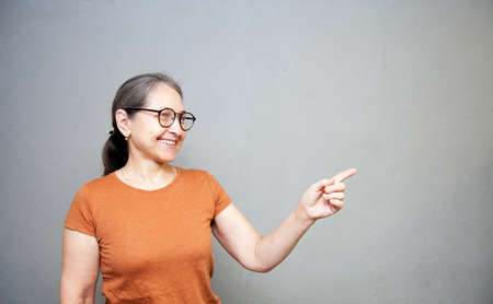 Elderly woman posing on gray background in glasses pointing to side with fingerの写真素材