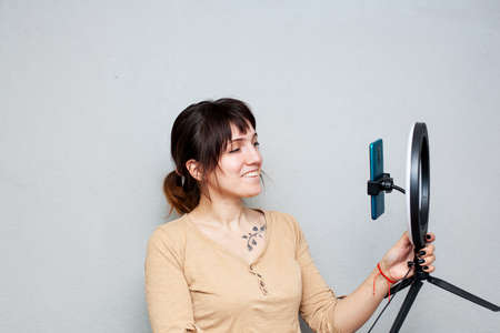 Girl with tattoo on collarbone recording video on smartphone and lighting herself with ring lamp on gray backgroundの写真素材