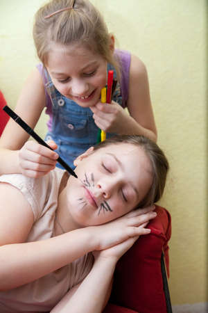 Girl drawing mustache on face of her sleeping sister. April fool's day