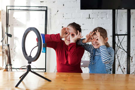 Joyful pre-teen girls posing for camera and making faces while recording video blog