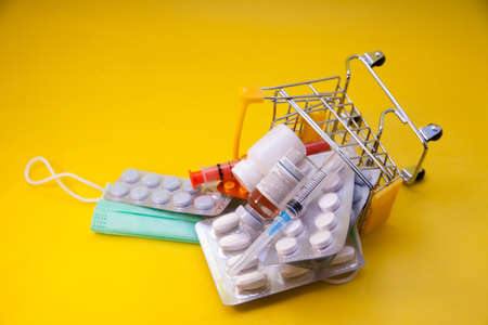 Pills and capsules in shopping cart on yellow background close-up. Concept of buying medicines online, home delivery of medicines during an epidemic.の写真素材