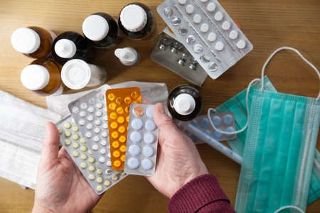 Close-up of elderly woman's hands with pills on background of medicines on table
