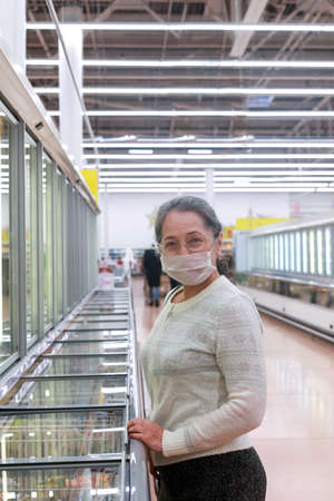 Senior female customer at department with freezing in supermarket wearing protective medical mask