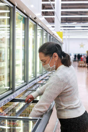 Woman wearing face mask shopping and choosing products in supermarket, active retired elderly people