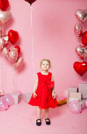 Portrait of three-year-old girl in red dress on pink background with gifts and balloons.の写真素材