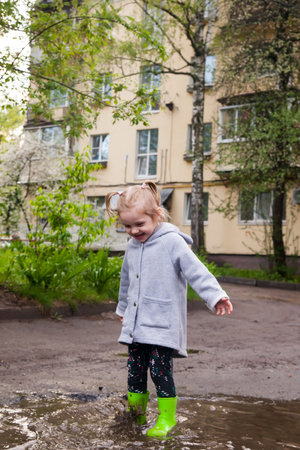 Spring portrait of baby in green rubber boots jumping through puddles.の写真素材